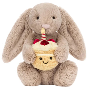 The Jellycat Bashful Beige Bunny 'Birthday' is an adorable plush toy holding a smiling cupcake with cherries and a striped straw—perfect as a birthday gift.