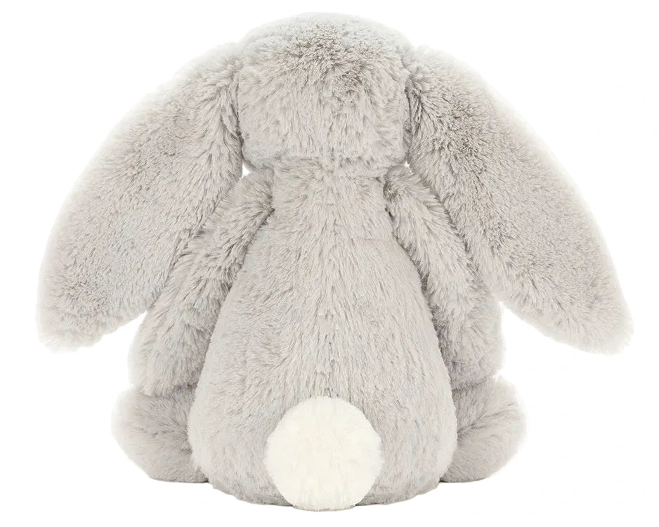 The Jellycat Bashful Silver Bunny plush, in light gray with long floppy ears and a round white tail, sits with its back to the camera—perfect as a bedtime story companion.
