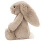 The Jellycat Bashful Bunny Beige Medium is a soft plush toy featuring a beige bunny with long floppy ears, black eyes, and a white tail, sitting upright and facing left.