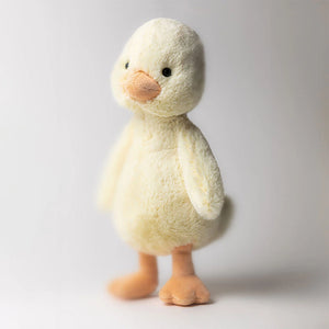 The Jellycat Bashful Duckling is a soft, yellow plush toy with an orange beak and feet, shown standing upright against a plain white background.