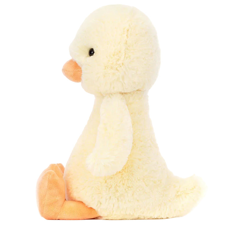 The Jellycat Bashful Duckling plush toy sits upright in side profile on a white background, featuring soft yellow fur and orange beak and feet.