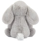 A plush grey Bashful Luxe Elephant Thuddeus from Jellycat sits facing away, highlighting its floppy ears and fluffy tail against a plain background.