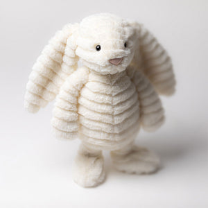 The Jellycat Bashful Luxe Bunny Nimbus, a plush white bunny with floppy ears and ribbed fur, stands upright against a plain light background.