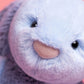 Close-up of Jellycat’s Puddlesea Bunny plush, featuring its soft light purple fur, textured nose, and shiny black eyes on a pink background—ideal to pair with beach toys or a sandcastle kit for creative play.
