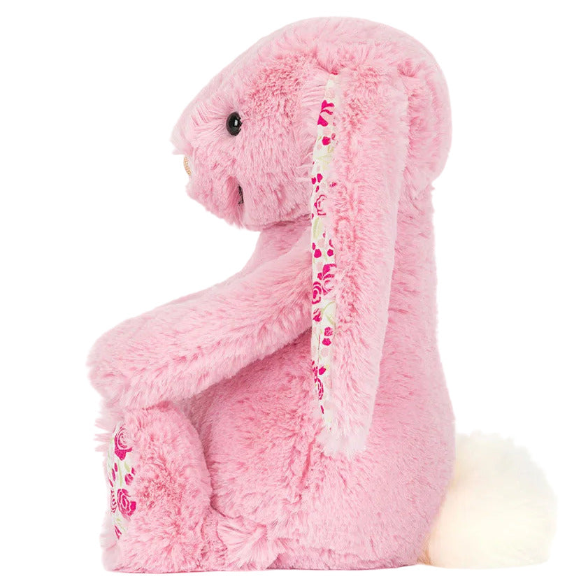 The Blushkin Blossom Luxe Bunny Original by Jellycat sits upright, displaying floral-patterned inner ears and feet, a white fluffy tail, and shiny black eyes.