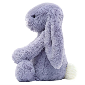 The Bashful Viola Bunny by Jellycat is a soft, plush toy with light purple fur, long floppy ears, black eyes, and a fluffy white tail, shown in side profile.