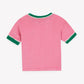 The Girls’ Livia T-Shirt by Bonton is shown laid flat with the back facing up. This short-sleeved style comes in a vibrant pink fiesta hue, featuring a green collar and sleeve cuffs highlighted by a white scalloped trim. Crafted from 100% cotton for all-day comfort.