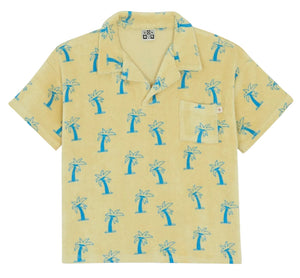 The Boys' Livio Polo, Palmiers by Bonton is a short-sleeve, light yellow 100% cotton shirt with a front pocket and blue palm tree patterns.