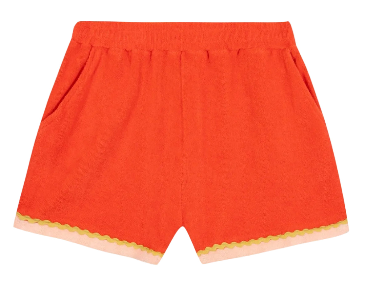 The Girls’ Livi Short by Bonton features bright orange terry cloth with an elastic waist, side pockets, and a wavy yellow croquet detail above a pale pink hem.