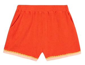 The Girls’ Livi Short by Bonton features bright orange terry cloth with an elastic waist, side pockets, and a wavy yellow croquet detail above a pale pink hem.