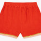 The Girls’ Livi Short by Bonton showcases bright red soft cotton terry cloth, viewed from the back, with an elastic waistband and pink trim accented by green wavy crochet detailing along the bottom hems.