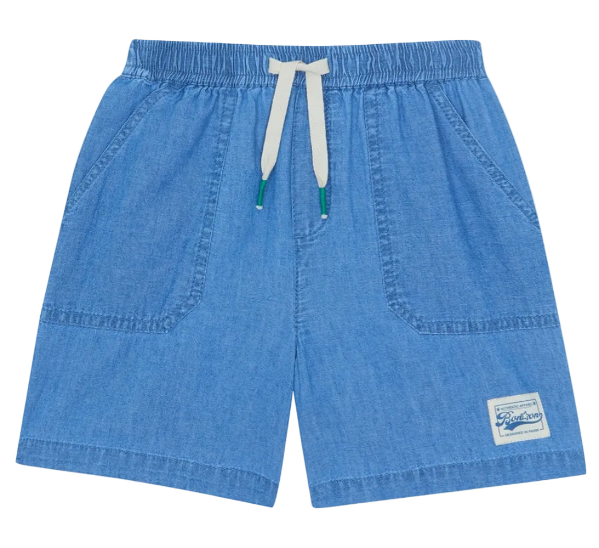 The Bonton Boys' Naples Short features light blue chambray, an elastic waistband with a white drawstring, two front pockets, and a sewn patch label—perfect for kids’ summer play.
