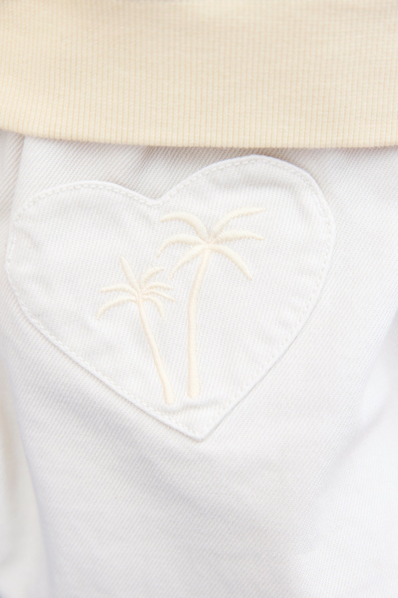 Close-up of a white heart-shaped pocket with embroidered palm trees beneath a beige ribbed waistband adds charm to the ecru Girls' Douchka Skirt by Bonton.