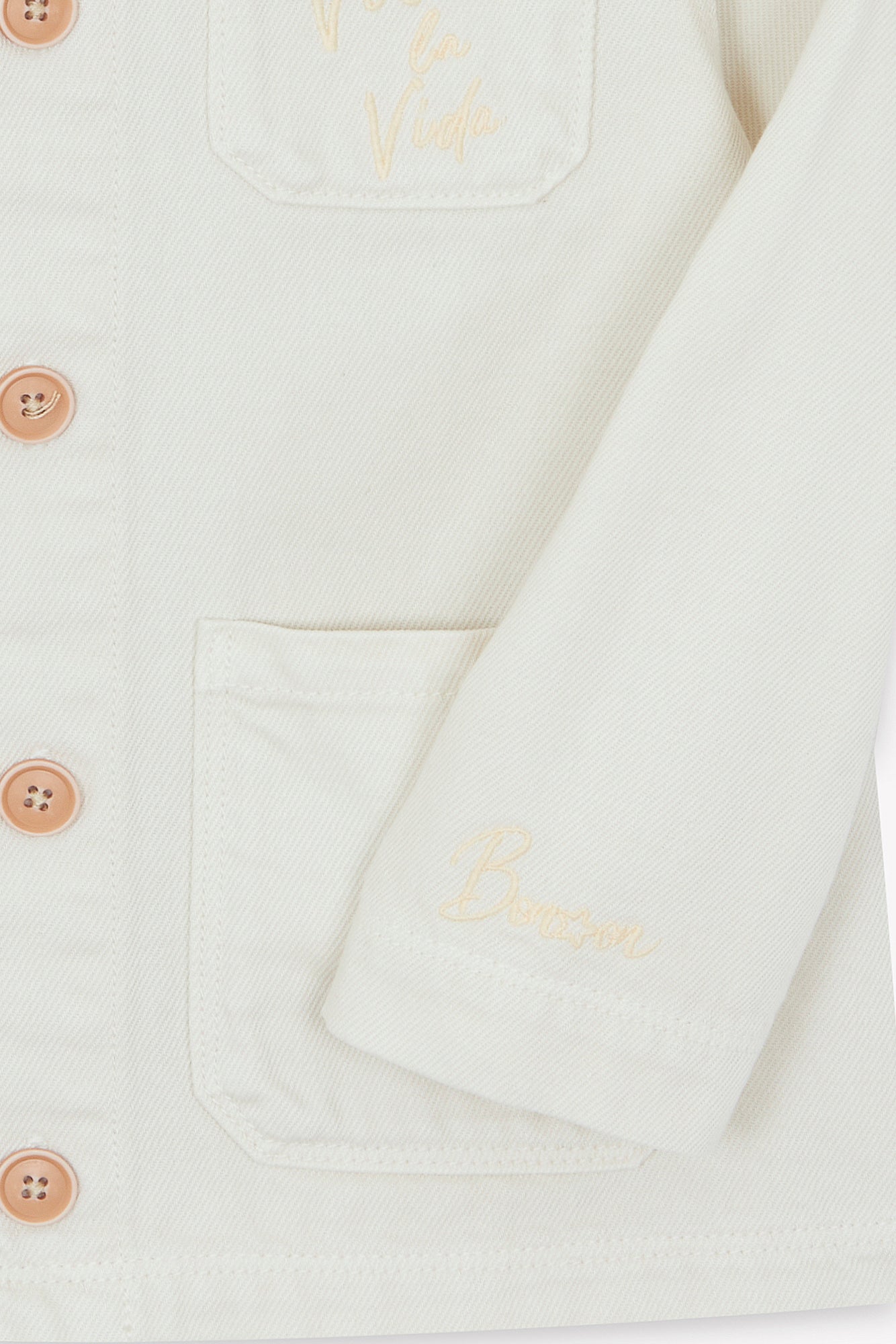 Close-up of the Girls' Ermana Jacket by Bonton in cream, showcasing a classic workwear style with tan buttons, two front pockets, and embroidered details on the pocket and chest.