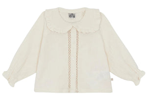 The Baby Girls’ and Toddler Fig Shirt by Bonton is a cream-colored long-sleeve shirt featuring a ruffled Peter Pan collar, front buttons, lace trim, and elastic cuffs, displayed on a white background.