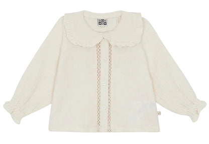 The Baby Girls’ and Toddler Fig Shirt by Bonton is a cream-colored long-sleeve shirt featuring a ruffled Peter Pan collar, front buttons, lace trim, and elastic cuffs, displayed on a white background.