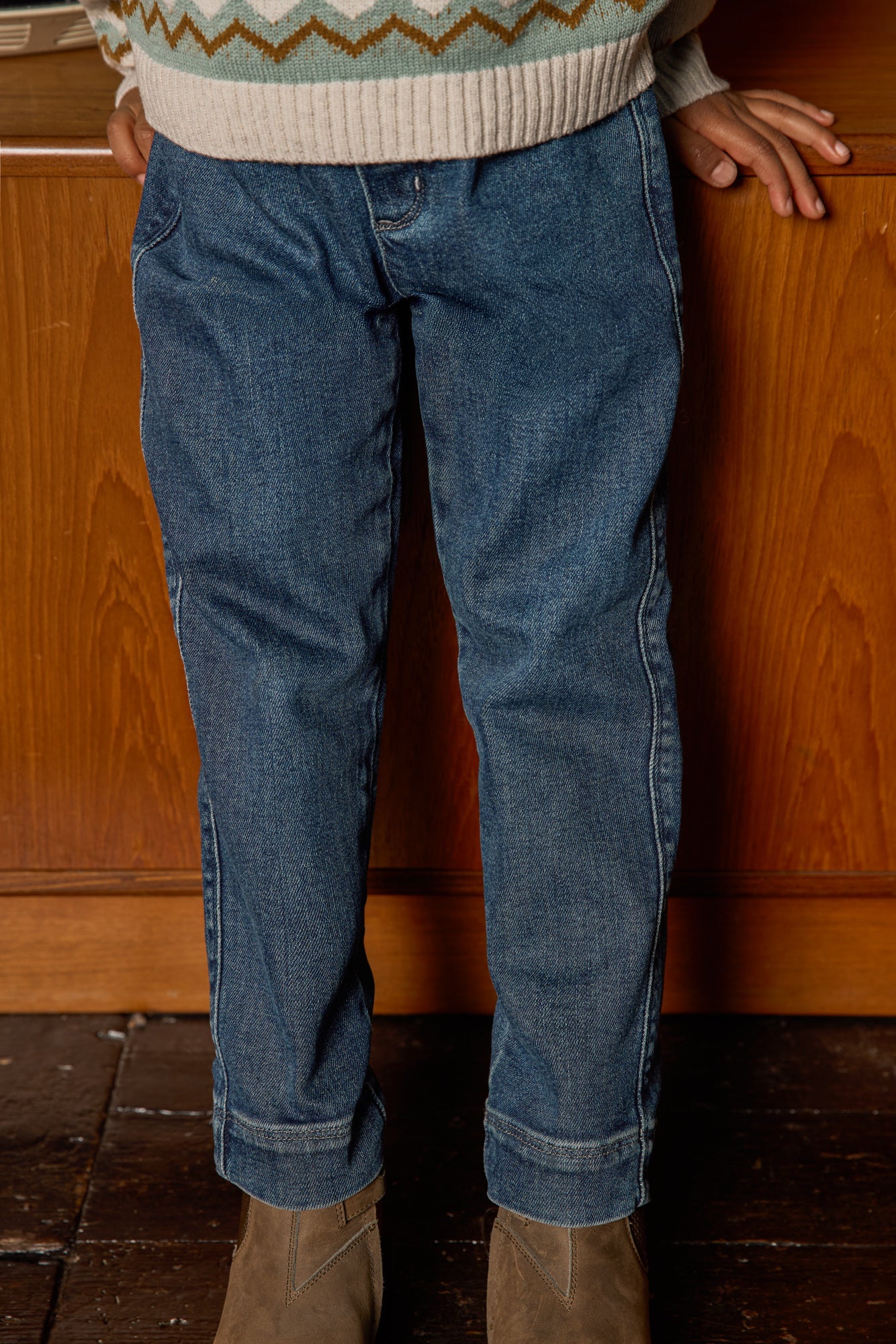 Bonton Boys’ Fracas Pant in mid-blue features straight legs, visible seam detailing, and an elastic waist for a comfortable, casual style. Shown paired with tan ankle boots and a fair isle knit sweater.