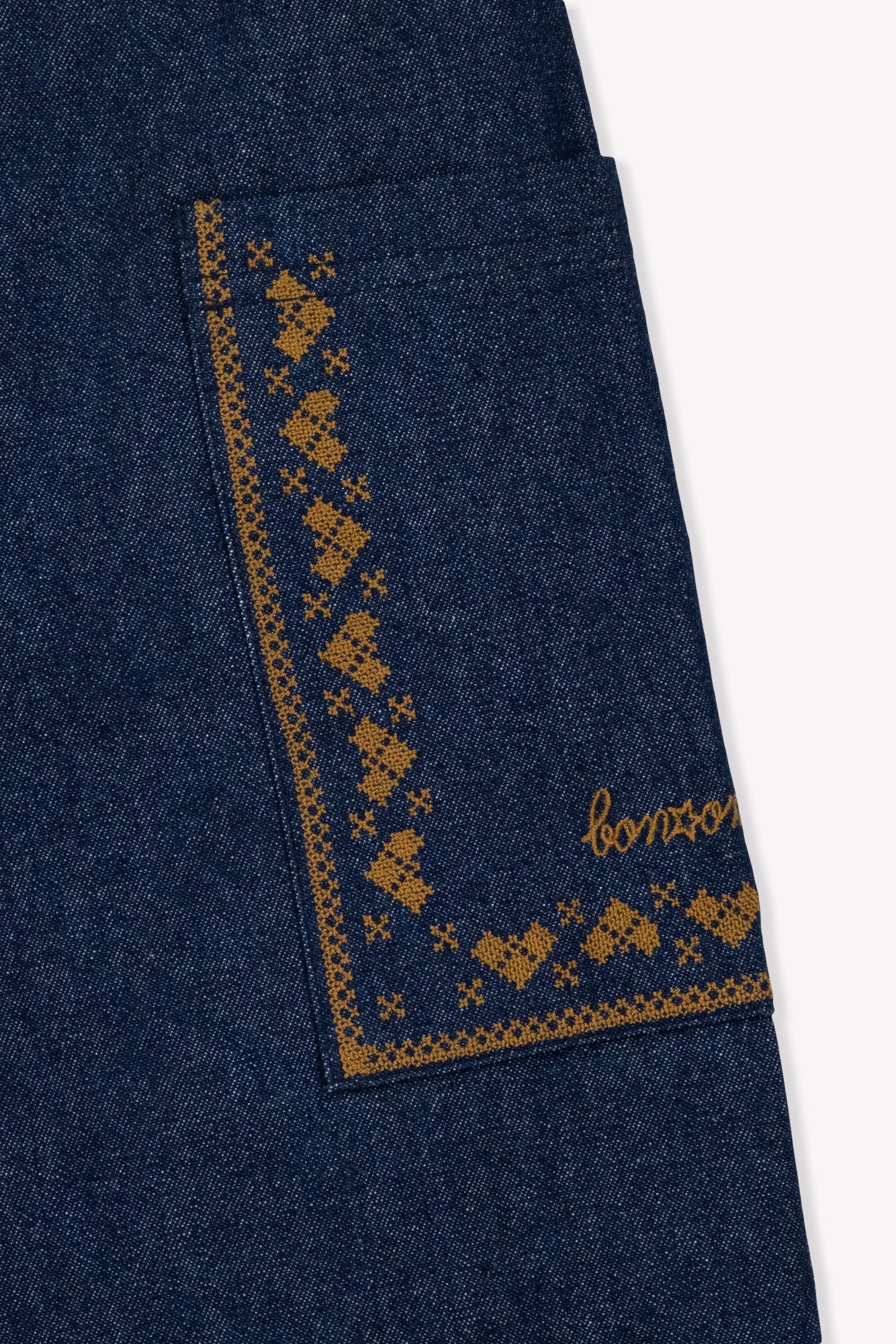 Close-up of the Bonton Girls’ Lauren Pant, highlighting a chambray cotton pocket detailed with mustard yellow embroidery and the word “bonjour” stitched in cursive.