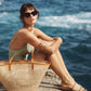 A person sits by the seaside wearing a swimsuit and sunglasses, with a woven tote bag and the Bembien Pia Slide sandals beside them, completing the perfect beach day ensemble.