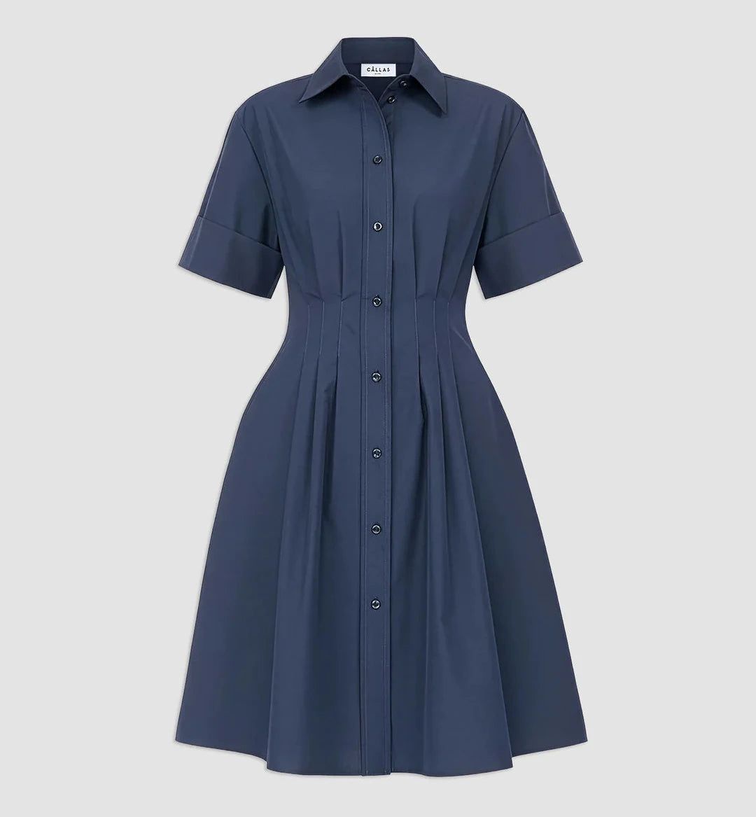 The Bergamo Dress by Callas Milano is a navy blue, short-sleeve, collared, button-down fit and flare cotton poplin dress with a pleated front and fitted waist, shown against a plain light gray background.
