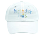 The Birthday Boy Baseball Hat by Bits & Bows is a white cap with "birthday boy" and a colorful cake embroidered on the front—a stylish way to celebrate while staying sun-safe.