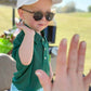 A young child in sunglasses, a green shirt, and a Bits & Bows Caddie Baseball Hat gets ready to high five an outstretched hand outside on a sunny day.