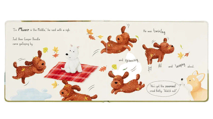 The "Munro in the Middle Book" by Jellycat is an illustrated children’s book featuring playful pups, including Cooper Doodle and Munro, frolicking around a white dog on a red checkered blanket, with falling leaves and a tan dog watching.