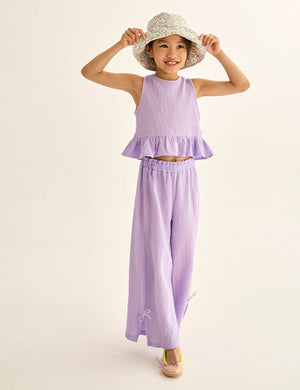 A young girl models Cozmo's Girls' Violet Wide Pants with a matching lavender ruffle-hem top and floral bucket hat, standing against a plain light background.