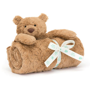 A plush tan teddy bear lays over a rolled brown blanket, secured with a white ribbon printed with "baby blanket" and teddy bear icons. This adorable Jellycat Bartholomew Bear Blankie makes a perfect gift for any little one.