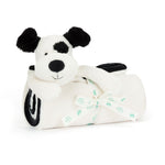 A Jellycat Bashful Black & Cream Puppy Blankie, this plush toy dog has soft fur and holds a rolled white blanket tied with a white ribbon featuring green text.