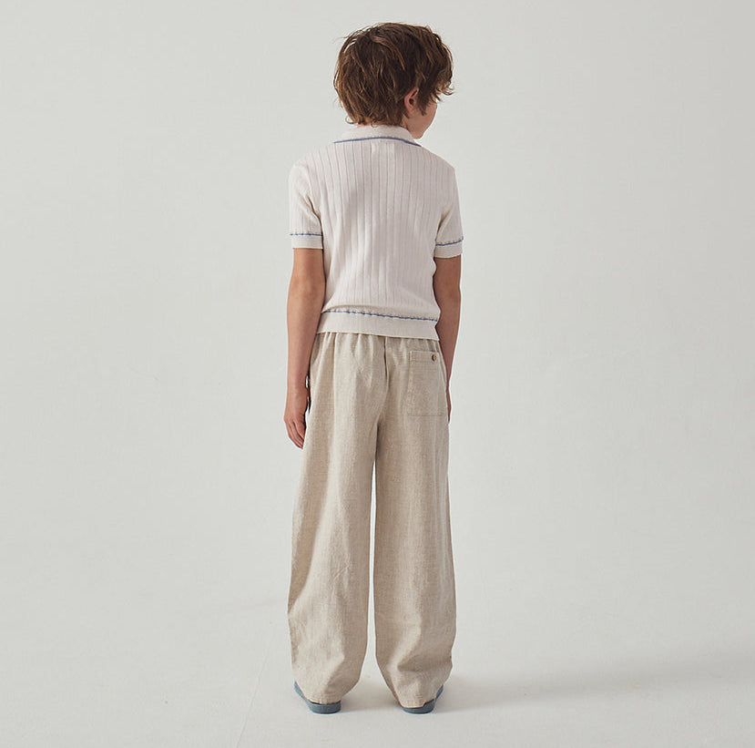 A child faces away from the camera, wearing a short-sleeved white shirt and loose-fitting Gingersnaps Boys' Erwin Drawstring Trousers in a natural colour, set against a plain white background.