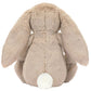 The Jellycat Blossom Beige Bunny 'Petal' sits facing away, displaying its long floppy ears and tiny white tail, as if lost in a daydream among wildflowers.