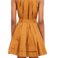 Woman wearing a sleeveless, mustard-colored Ulla Johnson Brienne Dress, Topaz crafted from cotton poplin, featuring gathered pleats and a flared skirt, viewed from the back. Adjustable strap ties add an extra touch of elegance to this stunning piece.