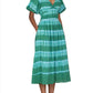 Person wearing an emerald tie-dye Banjanan Francesca Dress with puffed sleeves and a V-neckline. The midi-length dress is paired with brown sandals, and the person’s hands are in the dress pockets.