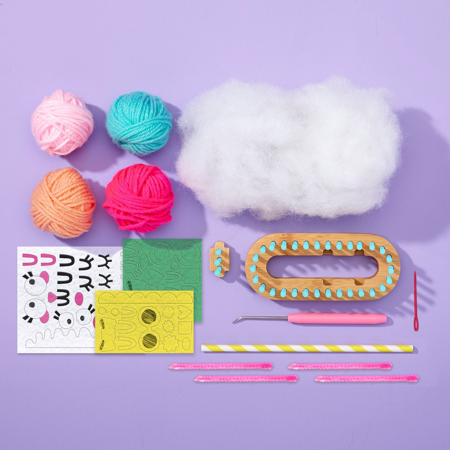Flat-lay of the Nimble Knitter - Squishee Stuffies craft kit by Bright Stripes on a purple background, featuring four yarn balls, stuffing, an adjustable knitting loom with a bamboo base, tools, felt face stickers, a straw, and pink pipe cleaners—everything you need to create adorable knit characters.