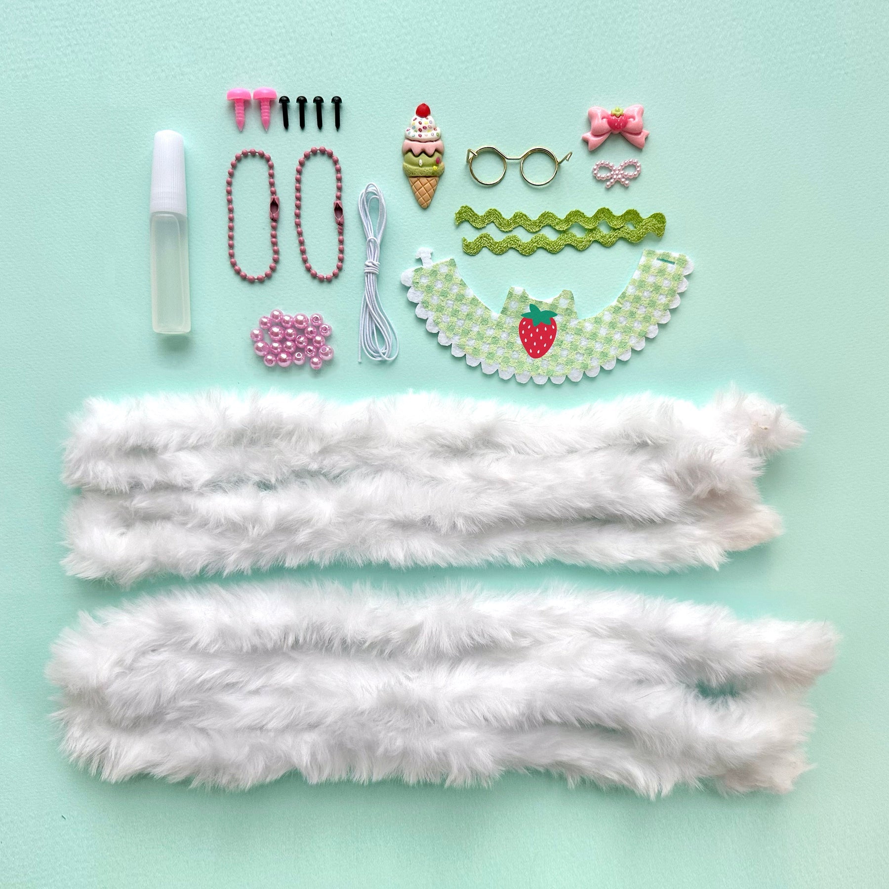 A flat-lay of DIY Chenille Cuties - Bunny Babes craft supplies from Bright Stripes on a light blue background, including glue, beads, doll glasses, a strawberry-print collar, and two lengths of white faux fur trim—perfect components for assembling your own DIY craft kit or making adorable bag danglers.