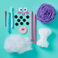 The Snack Knit Kit - Boba Buddy from Bright Stripes is displayed on a blue surface with yarn, knitting needles, felt circles, a needle, googly eyes, a patch, pipe cleaners, and polyester stuffing—everything you need for beginner knitting projects or to enhance your favorite craft kits.