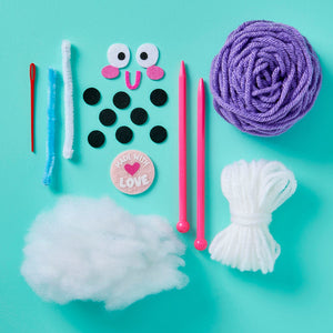The Snack Knit Kit - Boba Buddy from Bright Stripes is displayed on a blue surface with yarn, knitting needles, felt circles, a needle, googly eyes, a patch, pipe cleaners, and polyester stuffing—everything you need for beginner knitting projects or to enhance your favorite craft kits.