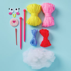 Colorful yarn bundles, plastic needles, a red needle, crafting eyes, a "Made With Love" badge, and polyester stuffing arranged on a light blue background—everything you need to begin knitting projects or start creating with the easy-to-use Snack Knit Kit - Cupcake Cutie from Bright Stripes.