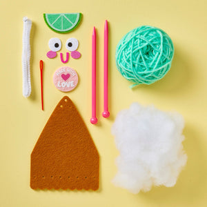 Introducing the Snack Knit Kit - Key Lime Pie by Bright Stripes: a beginner-friendly knitting kit featuring teal yarn, two pink needles, felt pieces, a "Made with Love" button, a pipe cleaner, a plastic needle, and stuffing—all beautifully arranged on a yellow background. Perfect for creative craft projects and fun knitting adventures!.