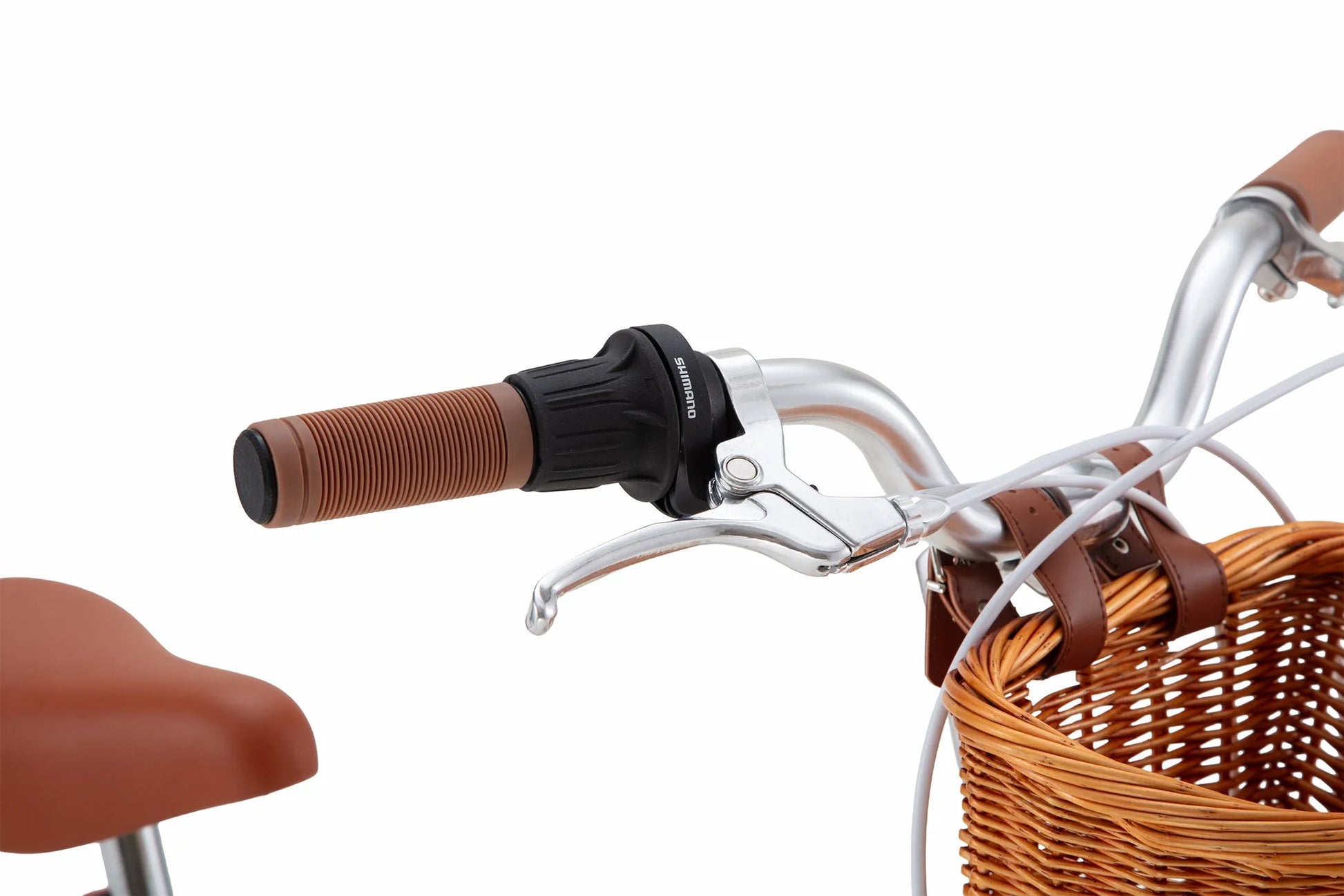Close-up of the Banwood Kids’ Vintage Classic Bike handlebar featuring a brown grip, brake lever, gear shifter, and a woven basket attached to the front—showcasing Scandinavian design influences. A portion of the matching brown saddle appears on the left, highlighting the timeless elegance inspired by vintage bicycles for children.