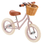 The Banwood Kids’ Vintage First Go Balance Bike is a charming pink bike featuring cream tires, a brown seat and handlebars, and a wicker basket attached to the front—perfect as your child’s very first kids’ bike.
