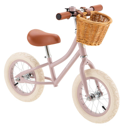 The Banwood Kids’ Vintage First Go Balance Bike is a charming pink bike featuring cream tires, a brown seat and handlebars, and a wicker basket attached to the front—perfect as your child’s very first kids’ bike.