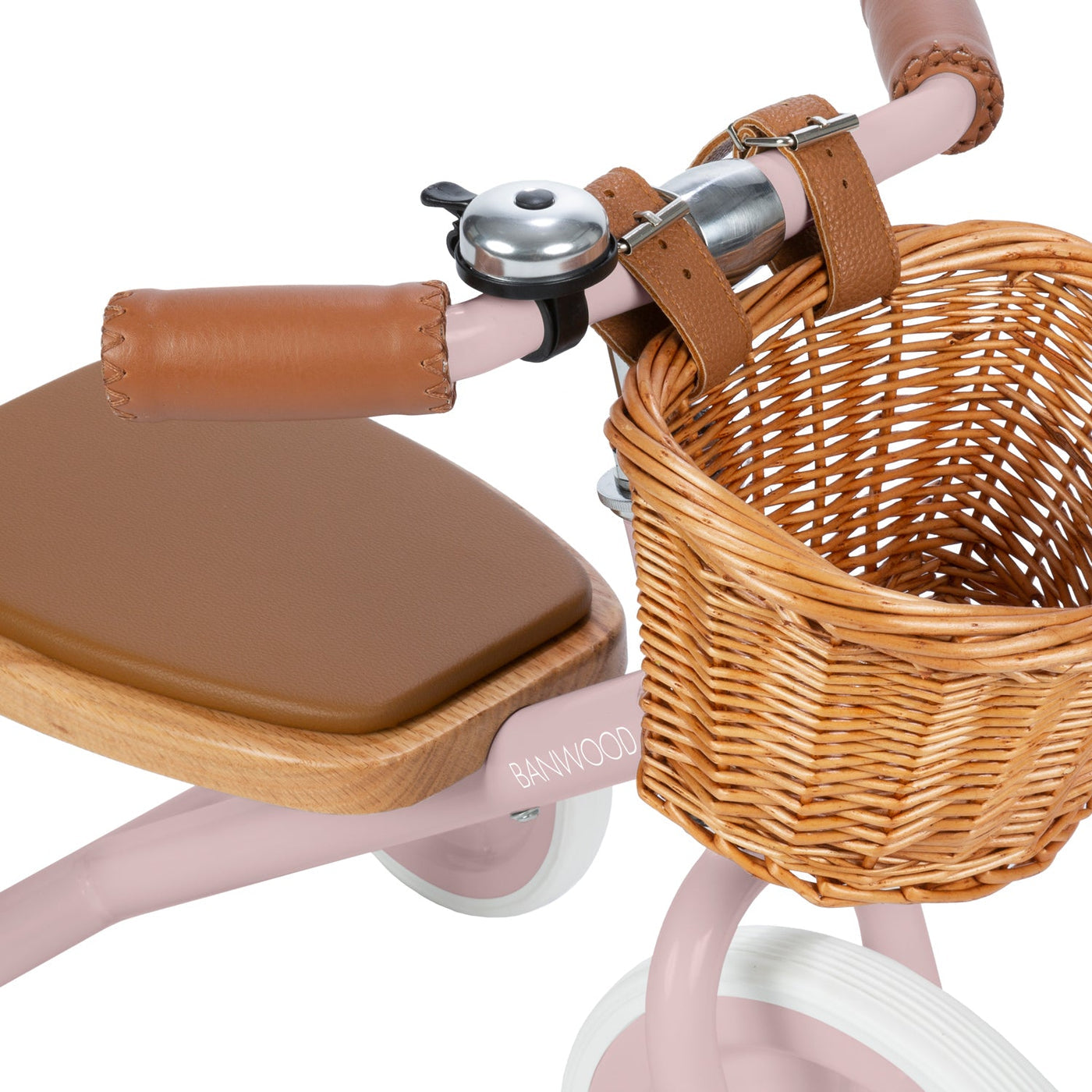 Close-up of the Banwood Kids’ Trike Vintage in pink, featuring a brown seat, leather handle grips, a wicker basket, and a silver bell on the handlebars.