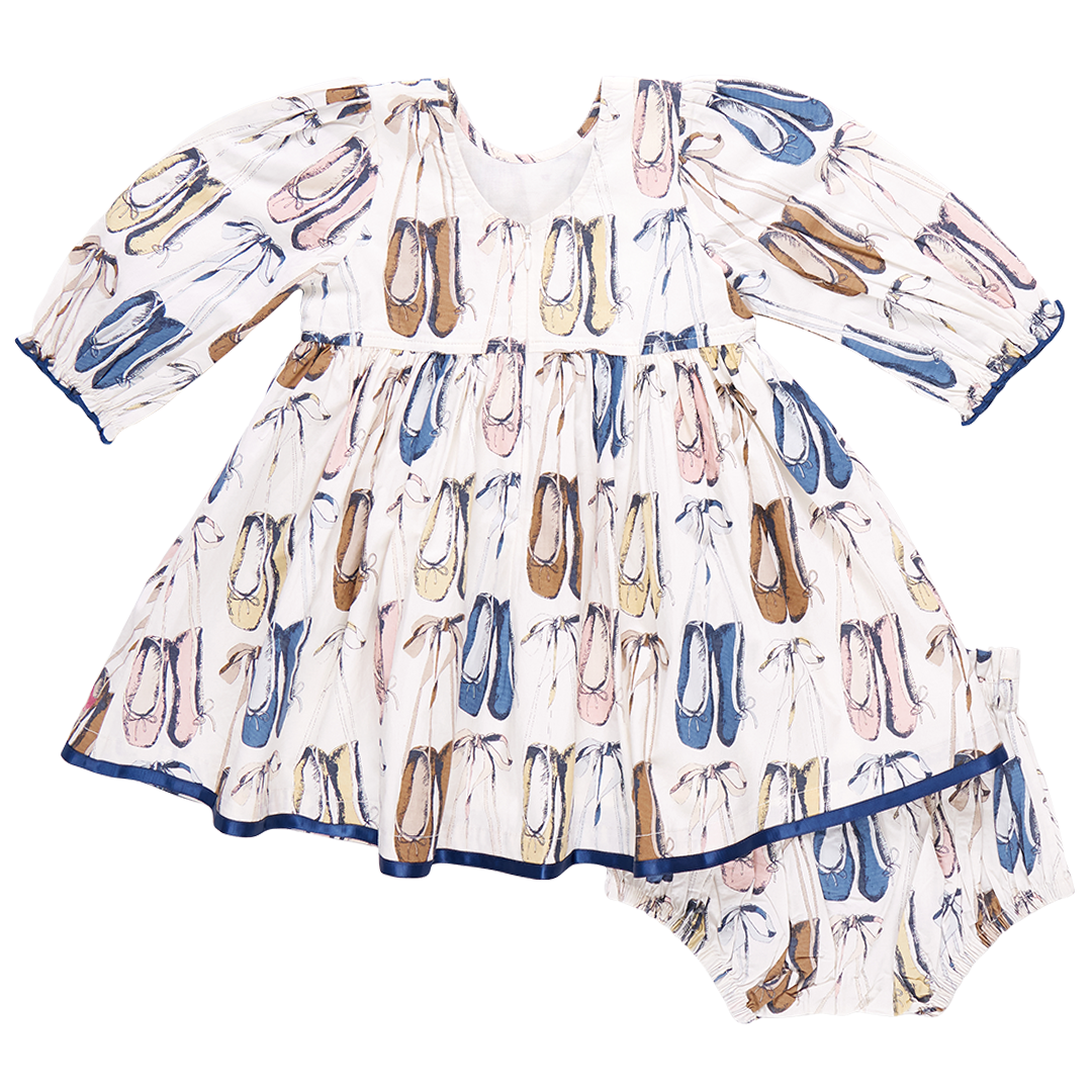 The Pink Chicken Baby Girls' Amma Dress is a charming addition to any little one's wardrobe, crafted from cotton poplin and showcasing a delightful pattern of illustrated shoes in various colors.