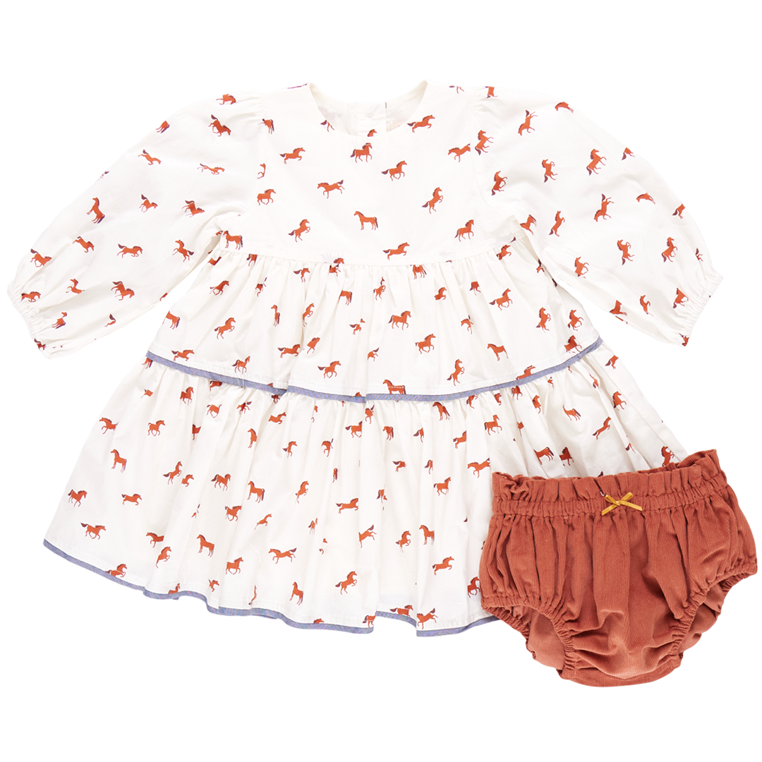 A baby girl's white long-sleeve Pink Chicken Julia Dress featuring a charming red horse pattern, paired with rust-colored bloomers adorned with chambray detailing.