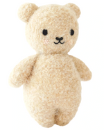 The Baby Boucle Bear - Honey by Cuddle + Kind is a beige, textured plush teddy crafted from heirloom-quality Peruvian cotton yarn, with black eyes, a stitched nose and mouth, and softly blushed cheeks.