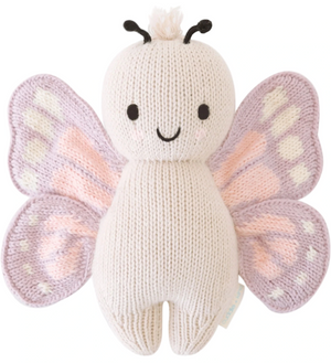 The Baby Butterfly by Cuddle + Kind is a hand-knit, heirloom-quality plush toy crafted from soft Peruvian cotton yarn with a white body, light purple and pink wings, black antennae, and a smiling face.