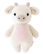 A knitted plush toy shaped like a strawberry cow, featuring a white and pink body, black eyes, beige snout, and small horns—expertly crafted by Cuddle + Kind from heirloom-quality Peruvian cotton yarn for softness and durability. This is the Strawberry Cow - Baby 7".