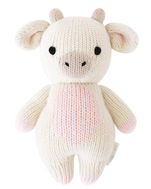 A knitted plush toy shaped like a strawberry cow, featuring a white and pink body, black eyes, beige snout, and small horns—expertly crafted by Cuddle + Kind from heirloom-quality Peruvian cotton yarn for softness and durability. This is the Strawberry Cow - Baby 7".